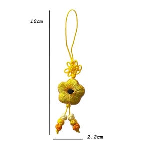 Pu&ograve; includere: Un ciondolo a forma di fiore ricamato giallo, lungo 10 cm e largo 2,2 cm. Il ciondolo presenta un fiore con un centro nero, un nodo decorativo e perline pendenti gialle, arancioni e bianche.