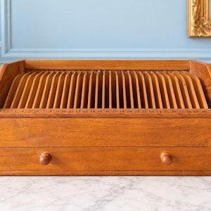 May include: A wooden desk organizer featuring a series of vertical slots numbered 1 through 31 along the front edge. The unit includes a single horizontal drawer at the base with two small round wooden knobs, providing a structured storage solution.