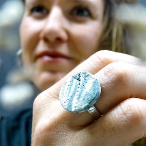 Könnte beinhalten: Nahaufnahme eines Rings mit einem runden, blauen und weißen Keramik Stein. Der Stein hat eine strukturierte Oberfläche mit weißen Punkten und Linien.