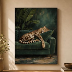 May include: A framed wall art print depicting a leopard with a spotted coat resting on a dark green velvet sofa. The leopard is positioned against a backdrop of large green tropical leaves, with one paw draped over a matching green cushion.