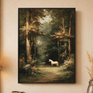 Op de afbeelding: Een ingelijste kunstdruk met een witte eenhoorn die op een zandpad in een dicht, donker bos staat. De scène toont hoge bomen met bruin en groen gebladerte, licht dat door het bladerdak valt en struikgewas op de voorgrond.