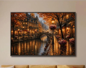 May include: A framed wall art print depicting a European canal scene at dusk with golden streetlights reflecting on the water, an arched stone bridge, multi-storey buildings, and trees with vibrant orange autumn foliage lining the cobblestone path.
