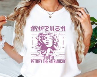 May include: White t-shirt with a graphic of Medusa, a mythical Greek figure with snakes for hair. The graphic is in purple and includes the text "MEDUSA" and "PETRIFY THE PATRIARCHY".