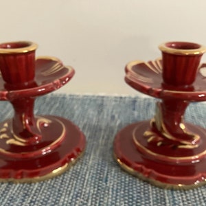 Może przedstawiać: Dwa czerwone ceramiczne świeczniki z złotymi akcentami. Świeczniki mają falisty wzór i podwyższoną podstawę.