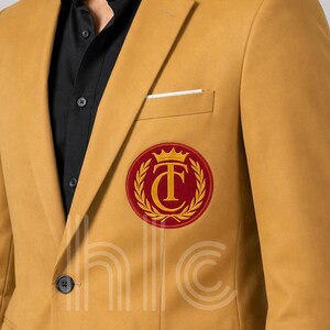 May include: Mustard yellow blazer with a black shirt underneath. The blazer features a red and gold circular emblem on the chest. A white pocket square is visible in the chest pocket. The blazer has a two-button closure.