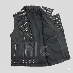 May include: Black leather vest with silver metal studs on the collar, shoulders, and lapels. The vest has a zipper closure, a belt with a buckle, and pockets. The interior lining is black.
