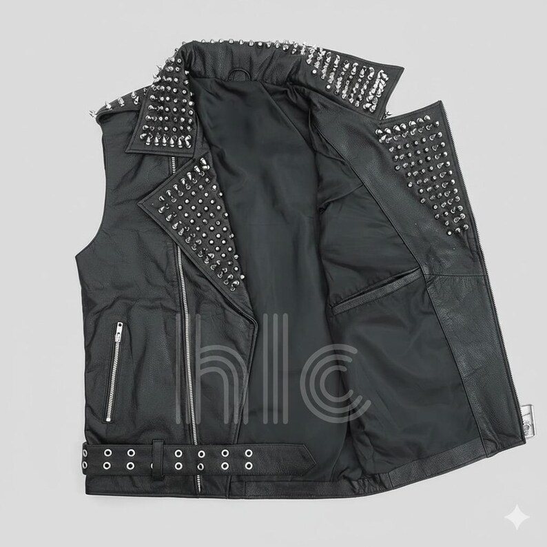 May include: Black leather vest with silver metal studs on the collar, shoulders, and lapels. The vest has a zipper closure, a belt with a buckle, and pockets. The interior lining is black.