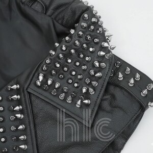 May include: Black leather jacket with silver cone studs on the collar and shoulders. The jacket has a classic biker style with a notched lapel and a fitted silhouette. The studs are evenly spaced and add a punk rock aesthetic.