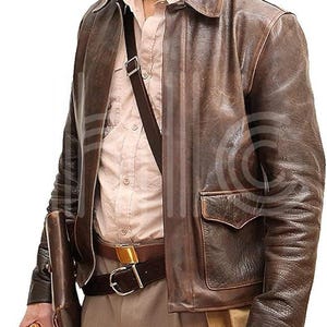 Könnte beinhalten: Braune Lederjacke mit Kragen und zwei Vordertaschen. Die Jacke wird über einem hellbraunen Button-Down-Hemd getragen und mit einem braunen Gürtel und khakifarbenen Hosen kombiniert. Eine Ledertasche und eine Peitsche sind ebenfalls zu sehen.