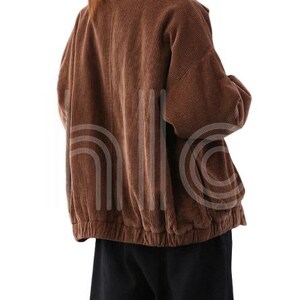 Puede incluir: Chaqueta de pana marr&oacute;n con cuello y dobladillo recogido. La chaqueta tiene mangas largas y un corte holgado. La tela tiene acanalado vertical. El modelo lleva pantalones negros.