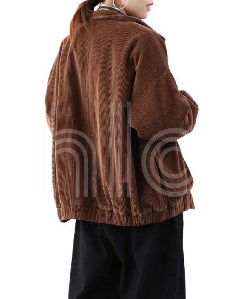 Puede incluir: Chaqueta de pana marr&oacute;n con cuello y dobladillo recogido. La chaqueta tiene mangas largas y un corte holgado. La tela tiene acanalado vertical. El modelo lleva pantalones negros.