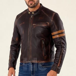 Puede incluir: Chaqueta de cuero marrón con cuello alzado, cierre de cremallera y dos rayas marrones en la manga izquierda. La chaqueta tiene un acabado envejecido y dos bolsillos delanteros. Estilo clásico.