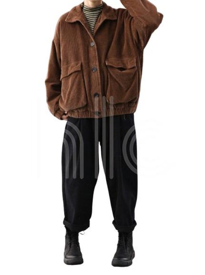 Puede incluir: Chaqueta de pana marr&oacute;n con grandes bolsillos delanteros y botones. La chaqueta se combina con pantalones negros y botas negras. El conjunto incluye una camiseta de cuello alto a rayas.
