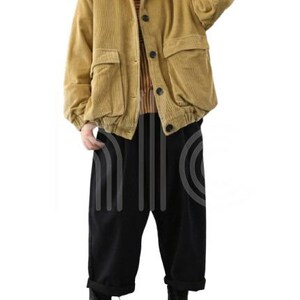 Puede incluir: Chaqueta de pana amarillo mostaza con grandes bolsillos delanteros y botones negros. La chaqueta se combina con pantalones negros de pernera ancha y botas negras. El conjunto es de estilo casual.