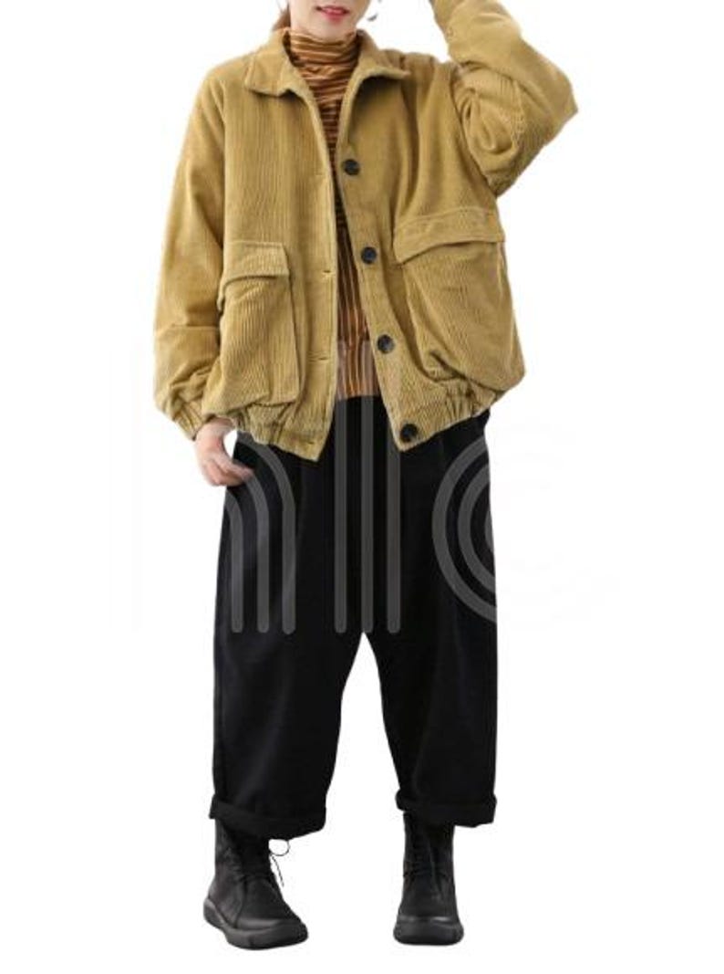 Puede incluir: Chaqueta de pana amarillo mostaza con grandes bolsillos delanteros y botones negros. La chaqueta se combina con pantalones negros de pernera ancha y botas negras. El conjunto es de estilo casual.