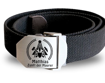 Op de afbeelding: Een zwarte canvas riem met een zilveren gesp. De gesp heeft een zwart-wit ontwerp van een kompas en gereedschap, met de tekst "Matthias Zunft der Maurer".