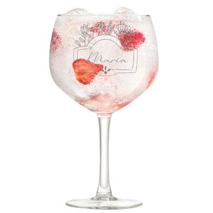 Puede incluir: Un vaso de ginebra de vidrio transparente con una inscripción personalizada que dice "Maria" con un diseño floral. El vaso está lleno de hielo y fresas.