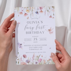 May include: A light-colored invitation with floral and fairy illustrations, held by hands. The text reads "Olivia's fairy first birthday" with the date August 28, 2025, and the time 3 PM-5 PM. The invitation includes an address and RSVP information.
