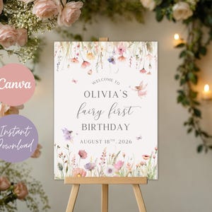 May include: A sign on an easel with the text "Welcome to Olivia's fairy first birthday August 18th, 2026". The sign has a floral design with pink, purple, and white flowers. The background is a soft cream color.