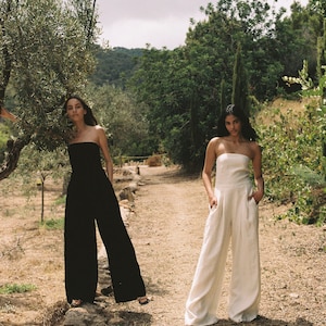 K&ouml;nnte beinhalten: Zwei Frauen in tr&auml;gerlosen Jumpsuits, einer schwarzen und einem wei&szlig;en, stehen auf einem Feldweg in einem Garten.