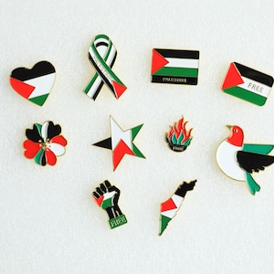 May include: A collection of enamel pins featuring the colors of the Palestinian flag. Designs include a heart, ribbon, flag, star, flower, flame, dove, fist, and a map of Palestine. Some pins have the word "FREE".