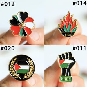 May include: A collection of four enamel pins with gold-colored borders. The pins feature various designs, including a flower, flames, a wreath with a flag, and a raised fist. Each pin has the word "FREE" on it.