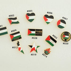 May include: A collection of enamel pins featuring the Palestinian flag and related designs. The pins include flags, hearts, and a star, with the text "FREE PALESTINE" on some. The pins are in various shapes and sizes.