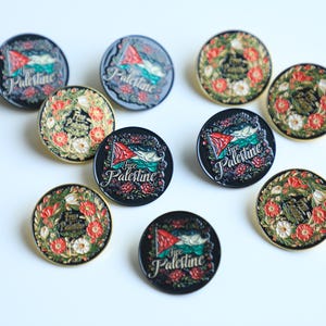 May include: A selection of circular badges displaying the Palestinian flag and floral patterns. Some badges include the text "Free Palestine". The badges are in black, red, white, green, and gold.
