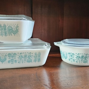 Könnte beinhalten: Drei weiße Auflaufformen mit Deckeln, die mit einem blauen und weißen Blumenmuster verziert sind. Die Formen sind pyramidenförmig auf einer Holzoberfläche angeordnet.