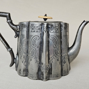 May include: A silver teapot with an ornate design and a wooden knob on the lid.