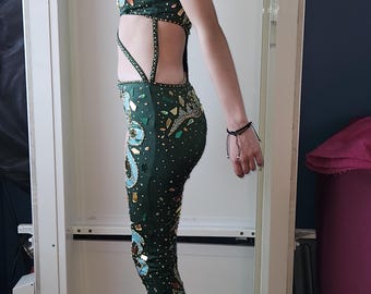 May include: A dark green, one-piece dance costume with intricate sequin and jewel embellishments. The costume features a halter top and leggings, with cut-out detailing on the sides. The sequins are gold, teal, and clear.