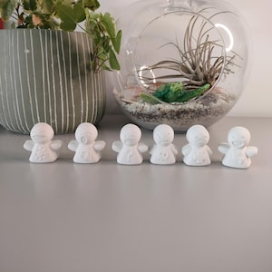 Puede incluir: Una colección de seis pequeñas figuras de cerámica blanca, cada una con una expresión facial diferente. Las figuras están dispuestas en fila sobre una superficie gris claro. Las expresiones varían de feliz a enfadado, mostrando una variedad de emociones.