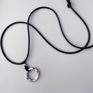 May include: A silver-colored pendant necklace with a twisted circular design. The pendant hangs from a black cord, knotted at the top and bottom. The necklace is displayed on a light gray background.