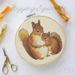 May include: Embroidered hoop art featuring two brown squirrels hugging. The squirrels are depicted in a realistic style with detailed fur and facial features. The hoop is made of wood and has a natural finish.
