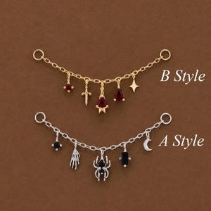 May include: Two decorative chain connectors with charms. B Style is gold-toned with a red stone, sword, and star. A Style is silver-toned with a black stone, skeleton hand, spider, and crescent moon. Both feature circular end loops.