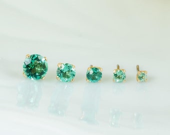 May include: Five pairs of emerald green gemstone earrings in different sizes, displayed on a white ceramic plate.