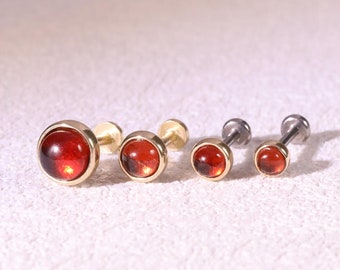 May include: Five gold and silver body jewelry pieces with red gemstone tops. The jewelry pieces are arranged in a row from largest to smallest.