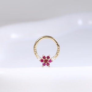 May include: A gold-coloured hinged ring earring featuring a flower design. The flower is made of small, round, red gemstones. The earring is set against a white background.