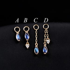 May include: Four pairs of gold-colored earrings with blue teardrop-shaped stones. The earrings are labeled A, B, C, and D. Some earrings have small clear stones or chain details. The earrings are displayed on a black surface.