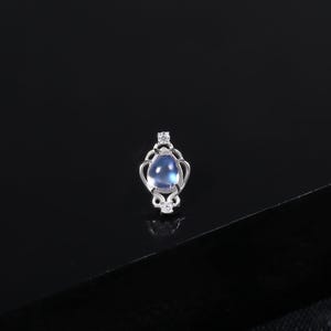 Peut inclure: Un petit pendentif argenté avec une pierre précieuse bleue clair en forme de goutte d'eau. Le pendentif présente un design ajouré orné de petites pierres d'accent claires. Le bijou est présenté sur une surface noire.