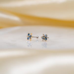 Puede incluir: Un par de pendientes de cuerpo dorados con piedras preciosas azules y transparentes. Los pendientes est&aacute;n engastados en un dise&ntilde;o de flor.