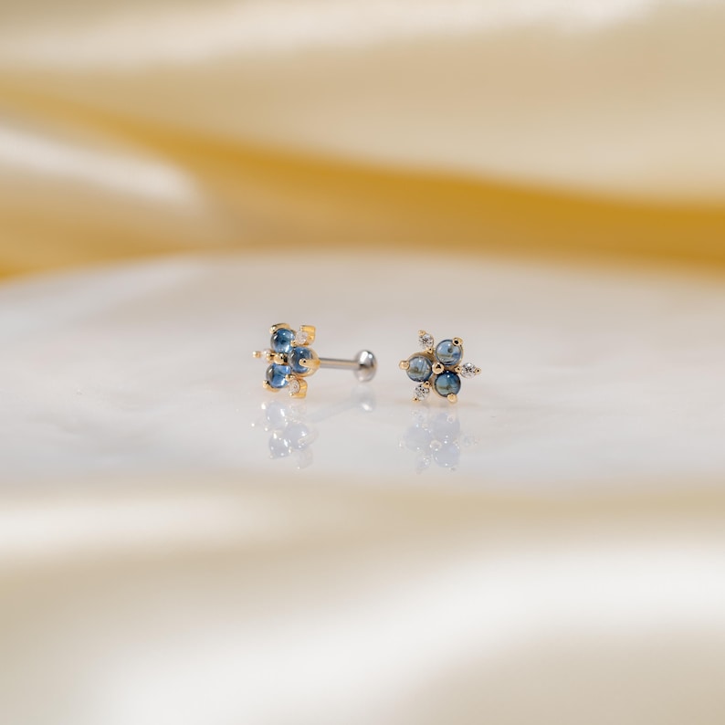 Puede incluir: Un par de pendientes de cuerpo dorados con piedras preciosas azules y transparentes. Los pendientes est&aacute;n engastados en un dise&ntilde;o de flor.