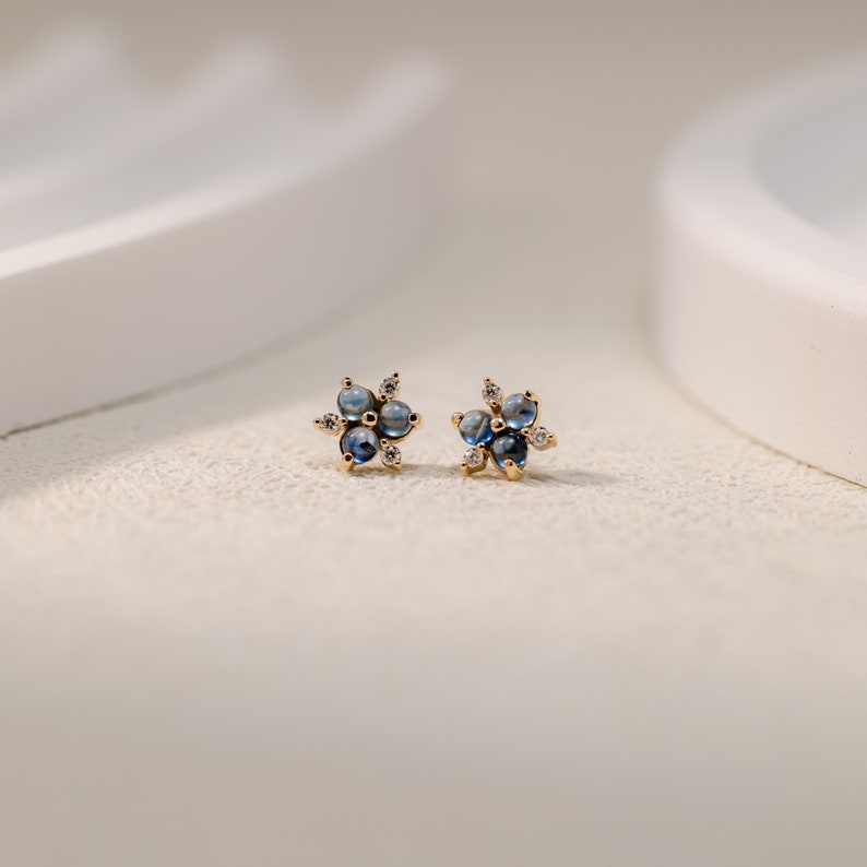 Puede incluir: Un par de pendientes de oro con un grupo de piedras preciosas azules y piedras preciosas m&aacute;s peque&ntilde;as transparentes en forma de flor.