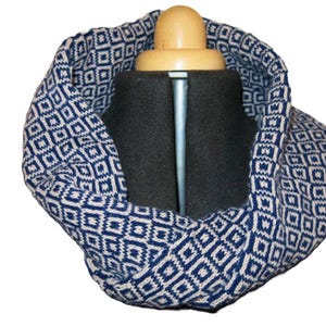May include: A blue and white knitted infinity scarf with a geometric pattern. The scarf is folded and displayed on a black mannequin.