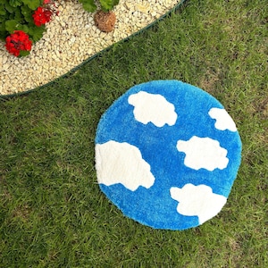 May include: A round blue rug with white fluffy clouds on it. The rug is on a green grassy lawn.