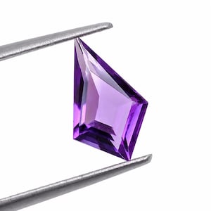 Könnte beinhalten: Ein facettierter Amethyst-Edelstein in Drachenform mit einem leuchtend violetten Farbton. Der durchscheinende Stein weist scharfe, geometrische Kanten und eine polierte Oberfläche auf und wird zwischen den Metallspitzen einer Pinzette gehalten.