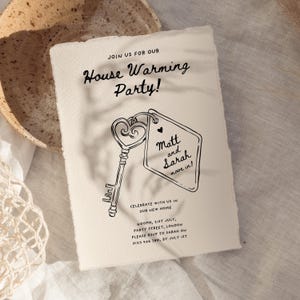 May include: A housewarming party invitation with a black and white illustration of a key and a tag that says "Matt and Sarah move in!" The invitation is on a cream-colored paper background.