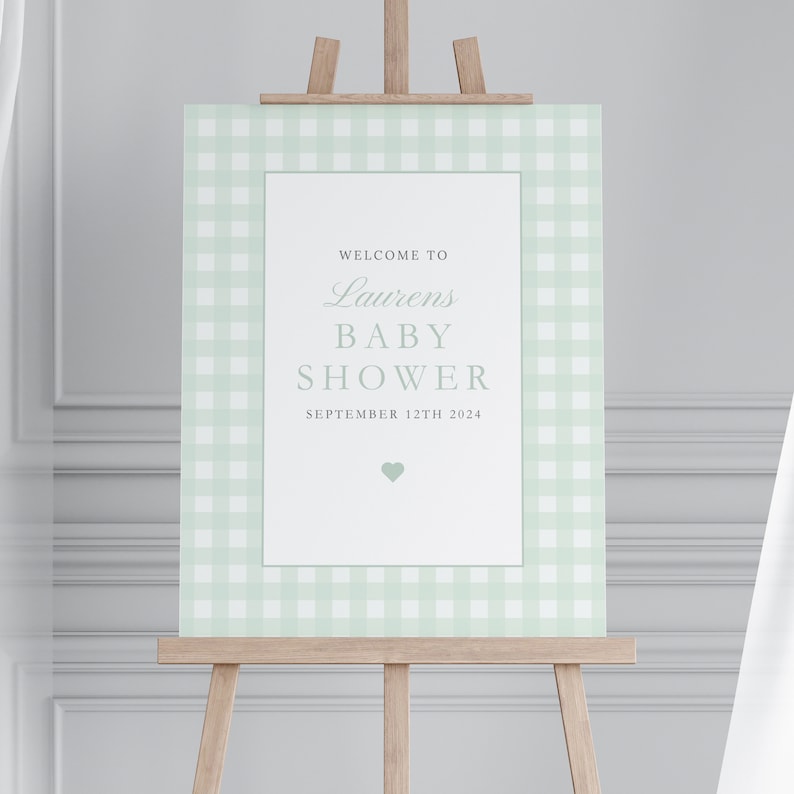 Puede incluir: Un cartel blanco con un borde de cuadros verdes. El cartel dice "Bienvenido a la Baby Shower de Laurens el 12 de septiembre de 2024" con un peque&ntilde;o coraz&oacute;n verde en la parte inferior.