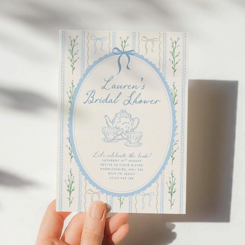 May include: A light blue and cream bridal shower invitation with the text "Lauren's Bridal Shower". The invitation features a blue oval frame with a teapot and teacups illustration. The background has a striped pattern with bows and floral accents.