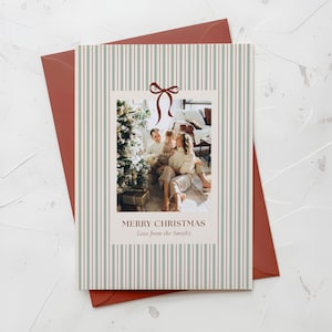 May include: A Christmas card with a family photo inside a striped border. The card features a photo of a family with a Christmas tree. The text reads "MERRY CHRISTMAS Love from the Smith's". The card is inside a red envelope.